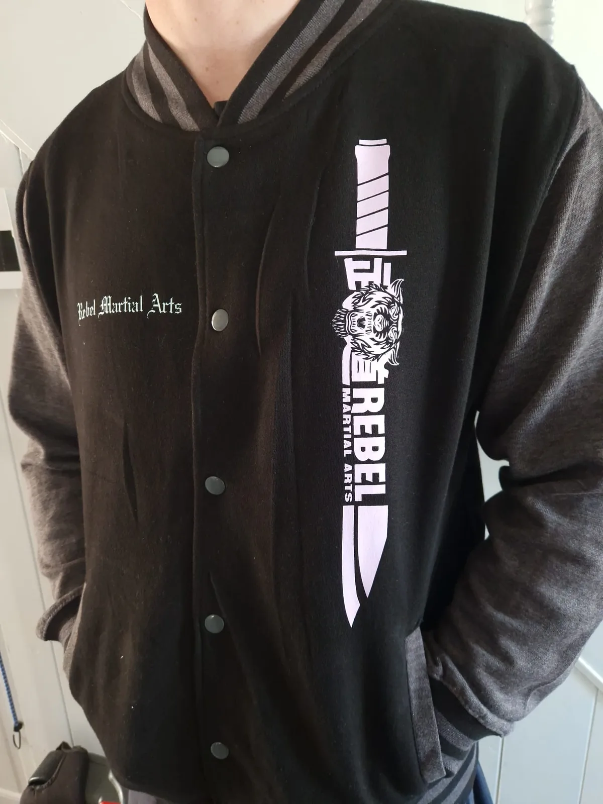 Rebel Martial Arts black varsity jacket worn to show the front design