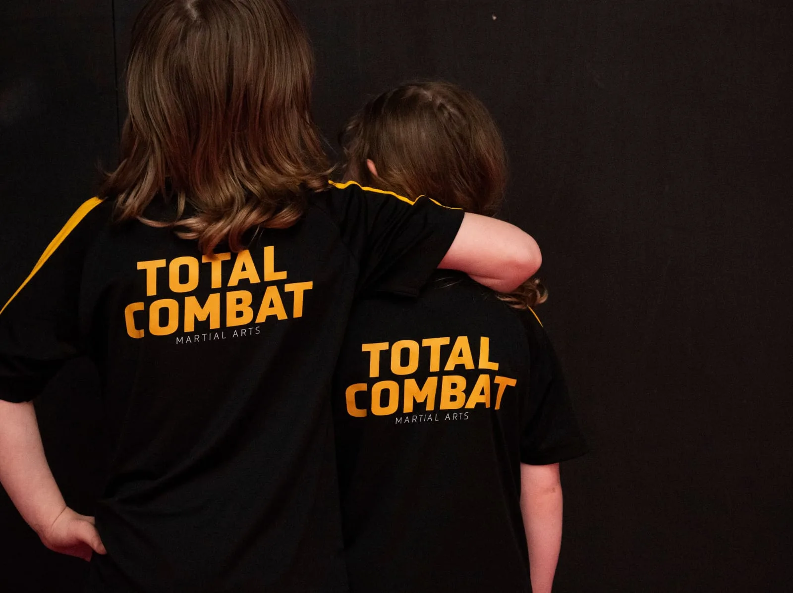 Two Total Combat members wearing black club t-shirts with yellow back printing